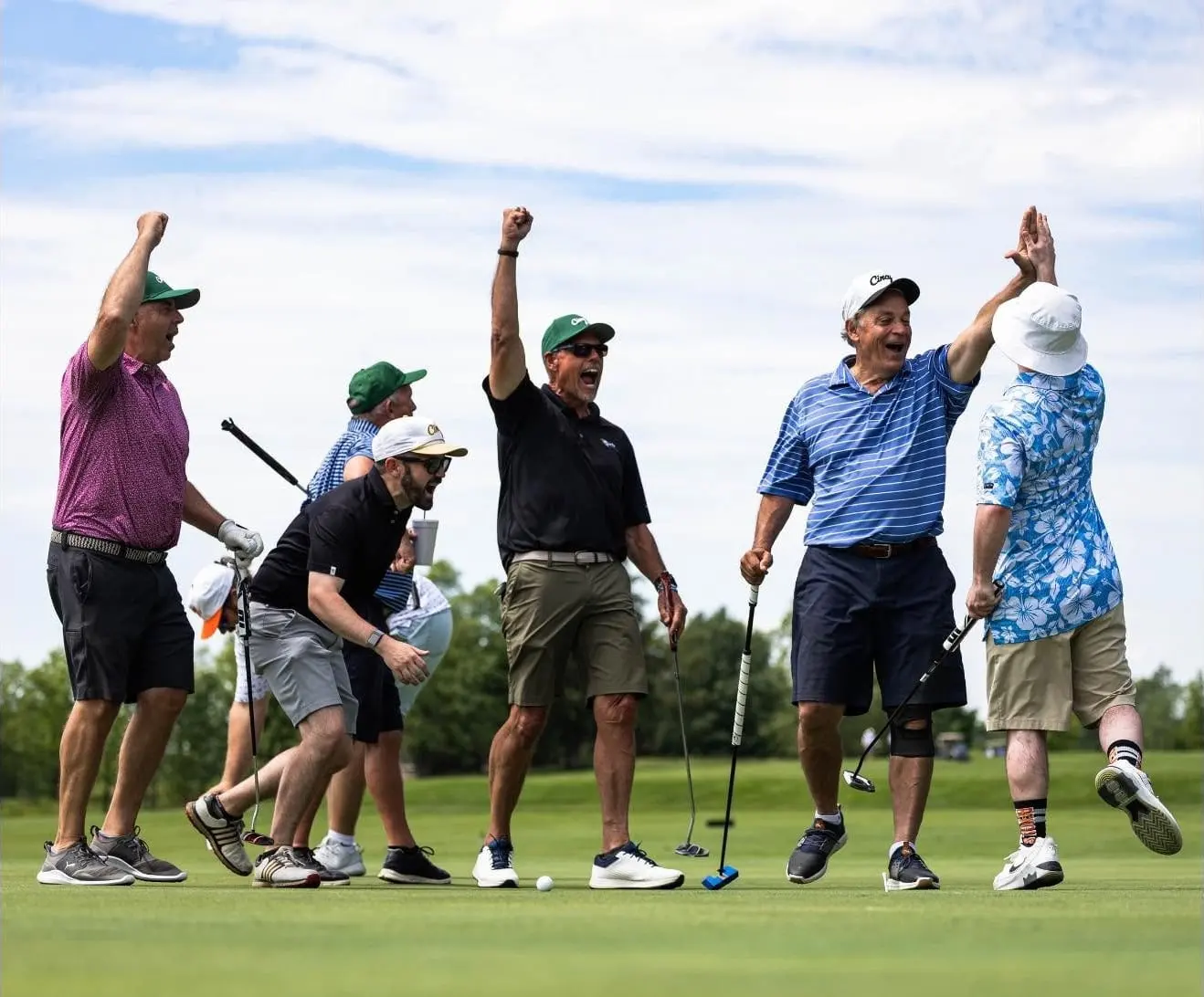 Golfers cheering and trading high-fives on a putting green under a summer sky