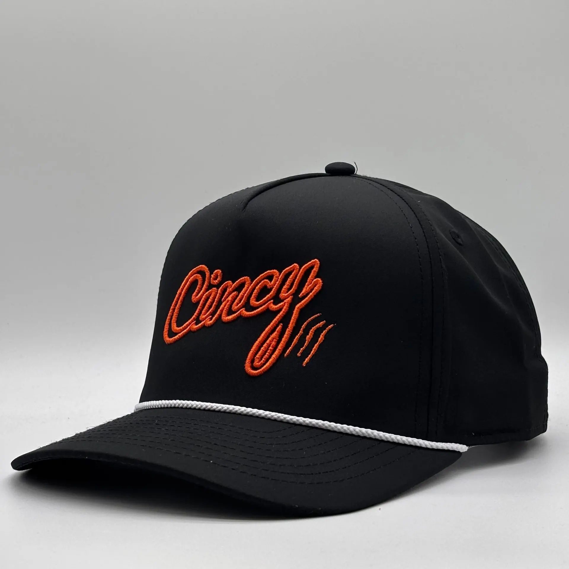 Black OG 5 Panel rope hat with orange 3D-outline Cincy script and claw slashes and a white rope across the brim, three-quarter view on a grey studio backdrop