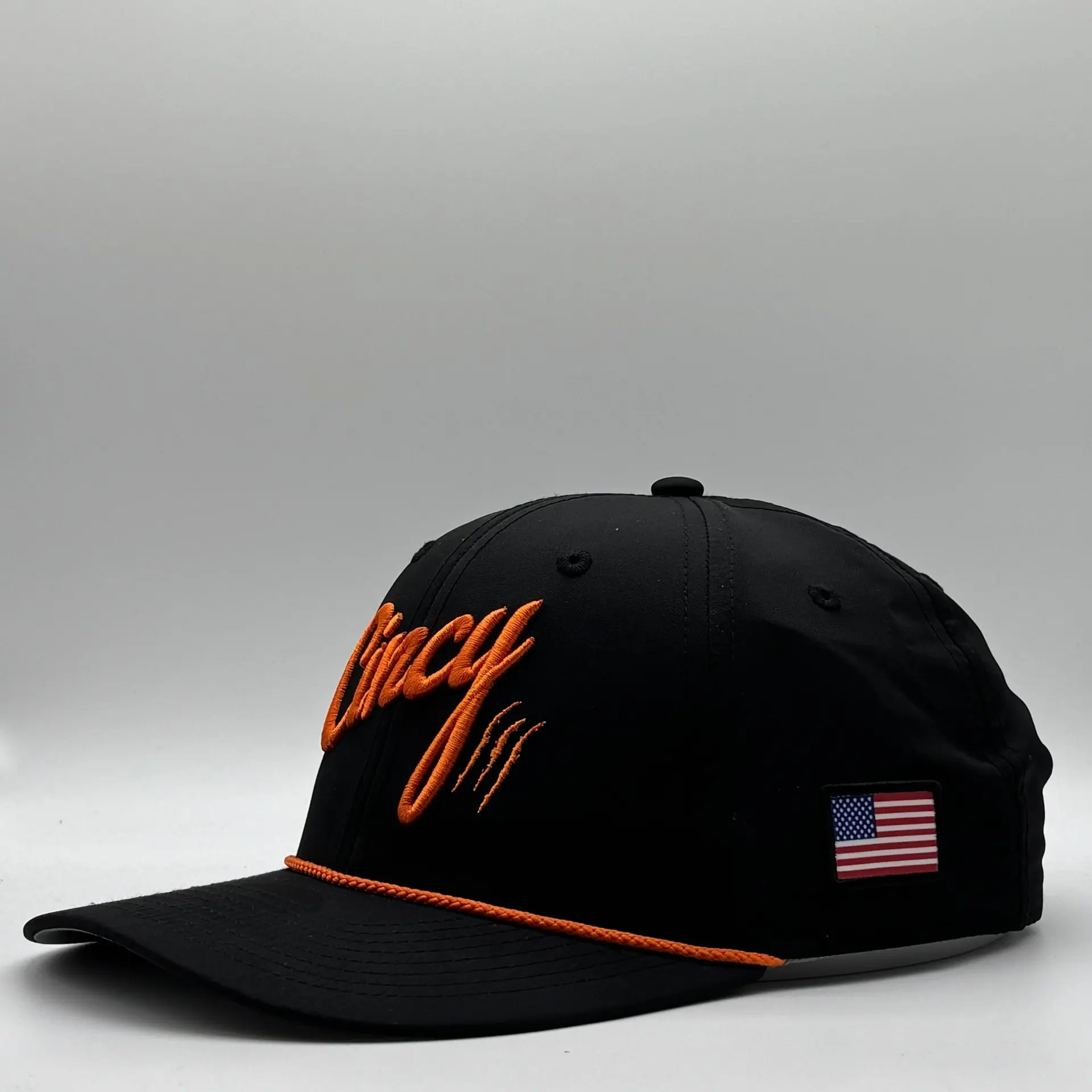 Side view of a black Mid-Crown rope hat with orange Cincy script, an orange rope across the brim and a small American flag patch